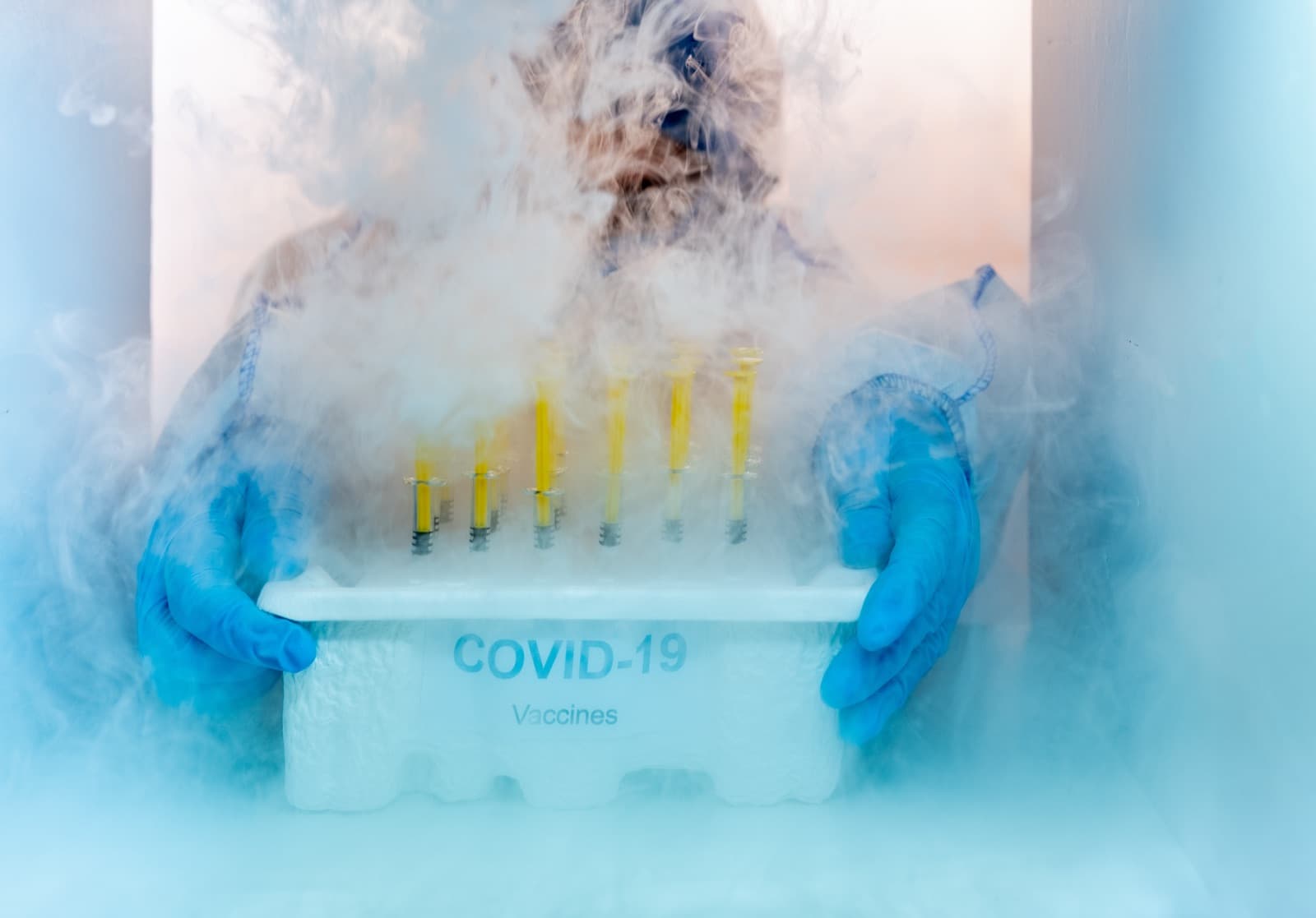 Gloved research staff in protective equipment handling a box of temperature-controlled specimen vials in a cold storage unit