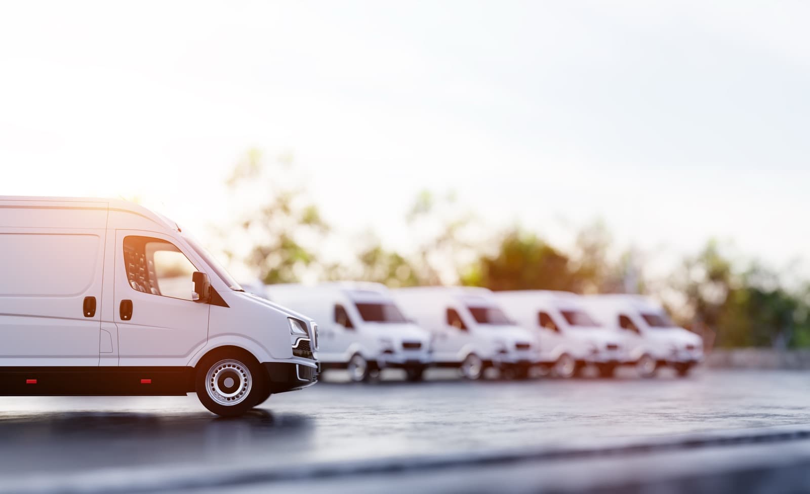 Row of enclosed white cargo vans on a lot, the vehicle type used for enclosed transport of instrument trays between healthcare facilities